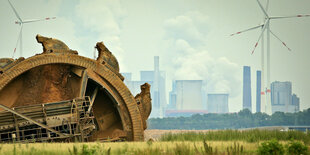 Ein Braunkohlebagger baggert im Tagebau Garzweiler, im Hintergrund steht ein Kraftwerk hinter Windrädern