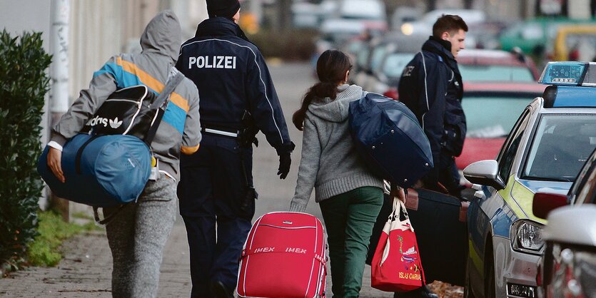 Zwei Polizisten bringen zwei Asylbewerber zu einem Polizeiauto.