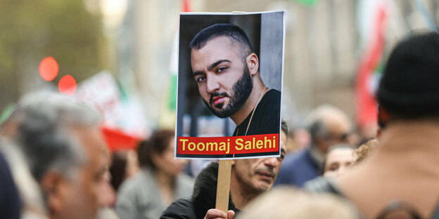 Ein Demonstrant hält ein Schild mit dem Porträt des Pappers Toomaj Salehi hoch.