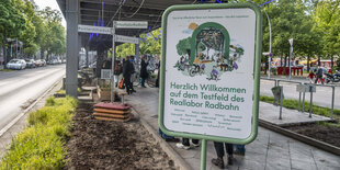 Ein Schild unter einem Hochbahnviadukt: "Herzlich Willkommen auf dem Testfeld des Reallabor Radbahn"