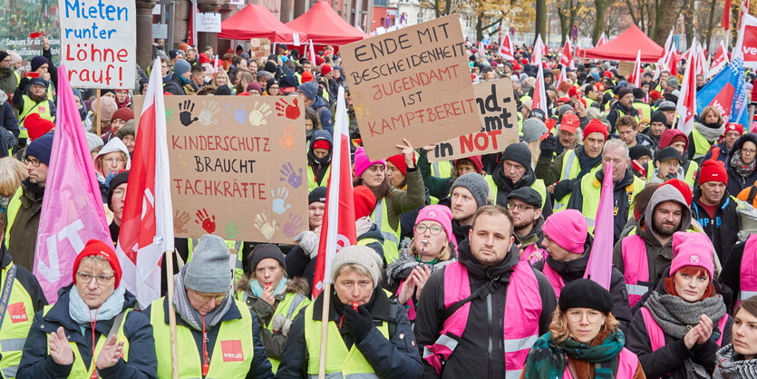 Menschen mit gelben und rosa Westen, einige halten ein Pappschild hoch, andere Fahnen