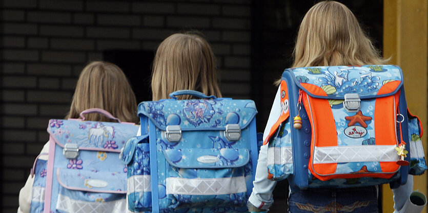 Drei Schulkinder mit Tornister gehen eine Straße entlang