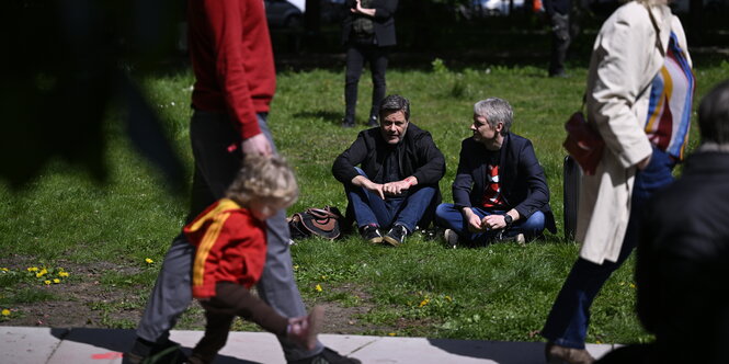 Robert Habeck sitzt mit einem Mann im Gras des Wesselparks.