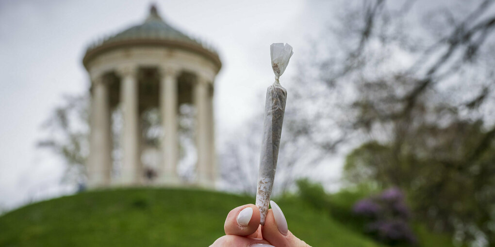 Frauenhand mit langen Nägeln hält Joint vor Kulisse des Monopteros im Englischen Garten München