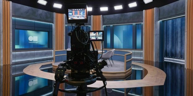 Ein Fernsehstudio mit einer großen Kamera, die vor Stühlen in der Mitte des Raumes steht