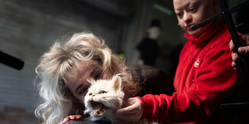 Zwei Schauspielerinnen schauen auf eine ausgestopfte Katze