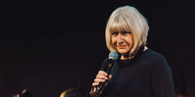 Eine Frau mit grauen Haaren hält ein Mikorfon in der Hand