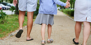 Ein Vater und eine Mutter halten die Hände ihrer Tochter, während sie auf einem Gehweg gehen