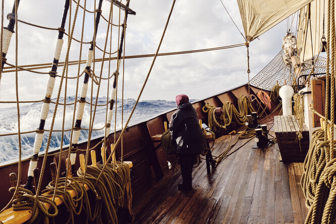 Eine Frau steht auf einem Segelschiff und schaut in die hohen Wellen