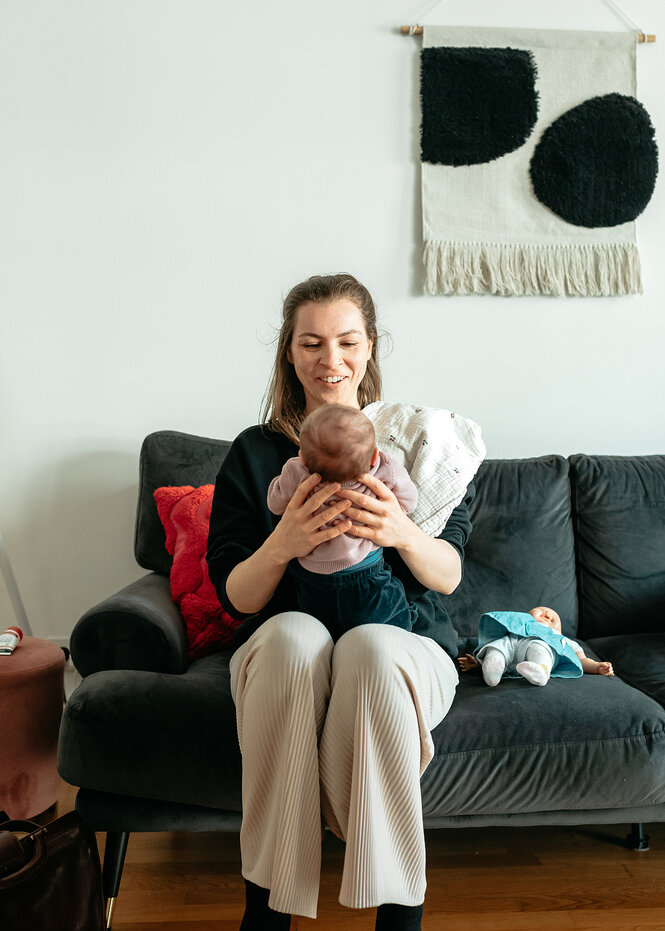 Eine Hebamme sitzt auf einem Sofa und hält ein Kind in den Händen