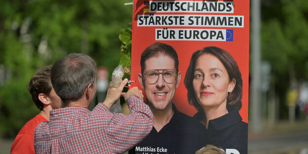 Ehrenamtliche hängen ein SPD-Wahlplakat auf.