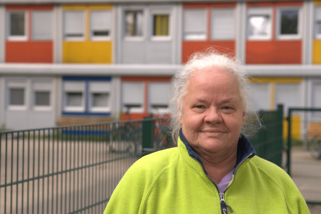 Eine ältere Frau in gelber Jacke vor einem Containergebäude