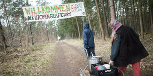 Aktivisten fahren Porridge und Geschirr von der Gemeinschaftsküche zu einem Camp der Initiative «tesla stoppen» in einem Kiefernwald nahe der tesla-Gigafactory Berlin-Brandenburg. Zwischen Bäumen ist ein großes Banner gespannt: "Willkommen in der Utopien-Gigafactory. No Cops, No Nazis, No Elon (A)".