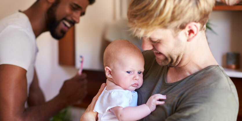 Zwei lachende Mnner, einer hält ein Baby