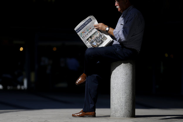 Ein Mann liest Zeitung und sitzt dabei auf einem Poller