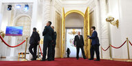 Mehrere Menschen stehen vor einer goldenen Tür, auf dem Boden liegt ein roter Teppich