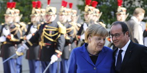 Angela Merkel und Francois Hollande stehen dicht beieinander und unterhalten sich, dahinter steht eine Militärgarde