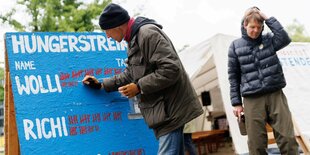 Zwei Männer stehen vor einem Plakat. Darauf zählen sie die Tage ihres Hungerstreiks.