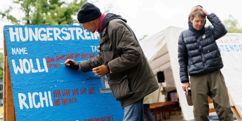 Zwei Männer stehen vor einem Plakat. Darauf zählen sie die Tage ihres Hungerstreiks.