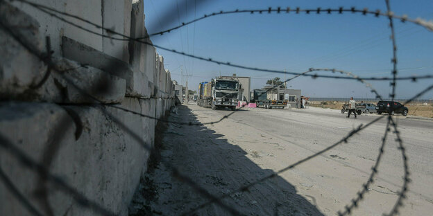 Stacheldraht an einer Betonmauer, im Hintergrund Lastwagen