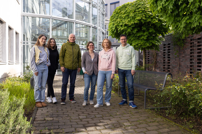 Sechs Menschen stehen im Hinterhof vor einem zylinderförmigen Glasbau