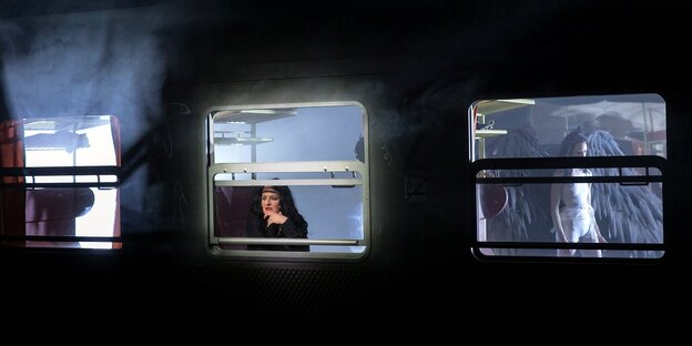 Bühnenbild: Nachtaufnahme eines Zuges, eine Frau schaut aus dem Fenster, durch ein anderes sehen wir eine Engelsfigur