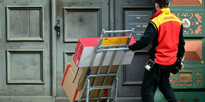 EIn Paketbote schiebt eine Sackkarre mit Paketen zu einem Hauseingang