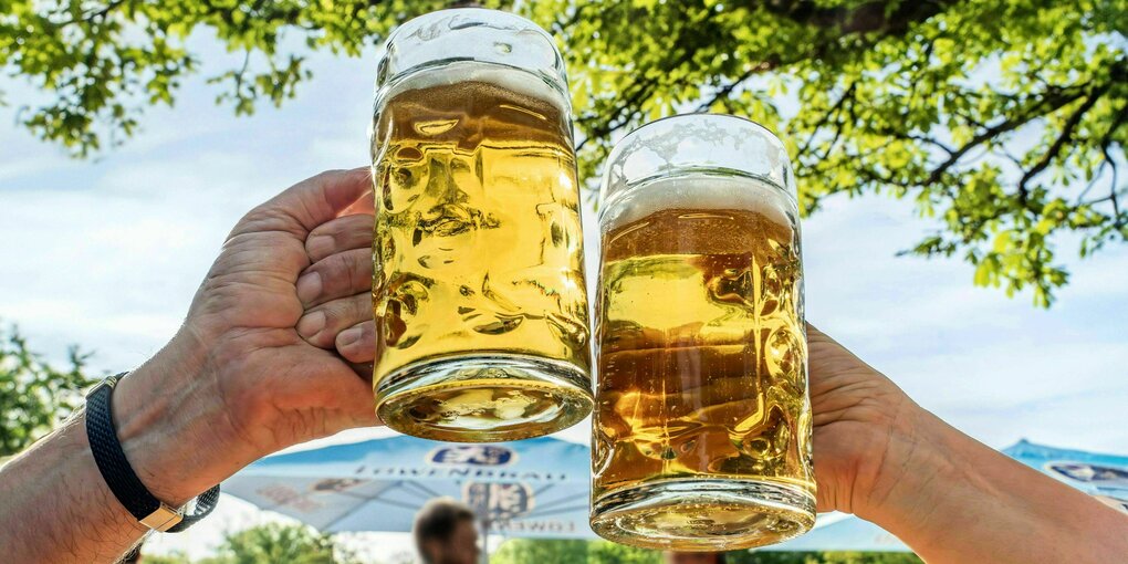 Zwei Biergartenbesucher prosten sich zu unter strahlend blauen Himmel