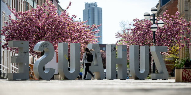 Das Wort "Zuhause" steht in großen Buchstaben als Installation vor Kirschbäumen