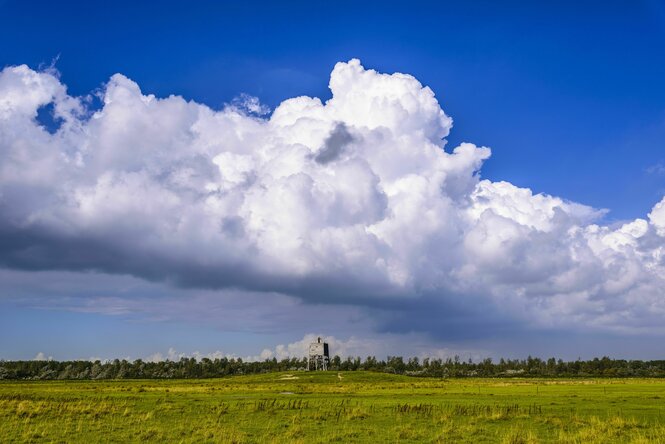 eine gewaltige Wolke hängt über einer Dünenlandschaft, ein Aussichtsturm ist in der Ferne zu erahnen