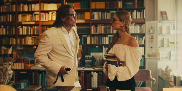 Zwei weiß gekleidete Menschen stehen in einem Raum mit einem Bücherregal