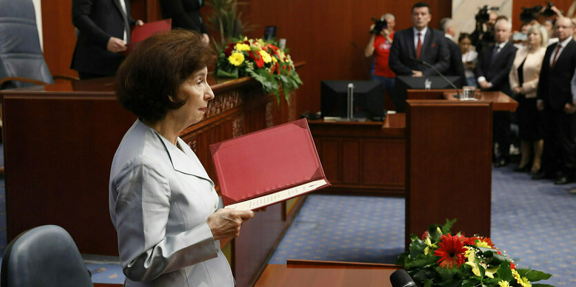 Gordana Siljanovska Davkova steht vor einem Tisch mit einer roten Mappe in der Hand im Parlament