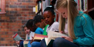 Kinder sitzen in einer Reihe auf dem Boden und lesen.