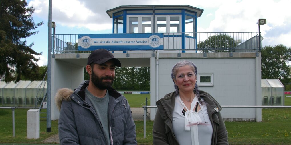 Ein Mann und einer Frau stehen vor einer Sportstätte