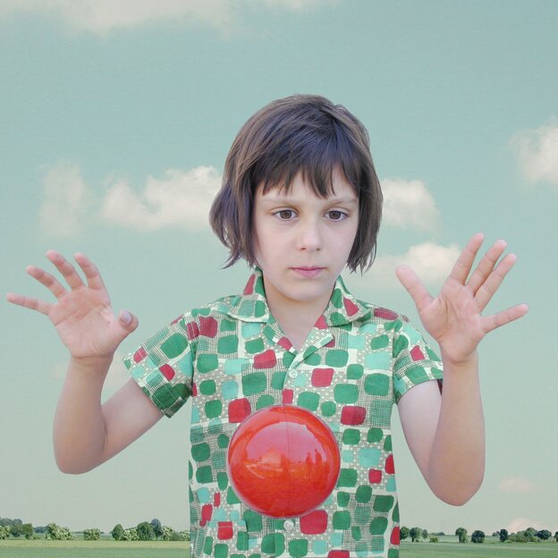 Foto von einem Mädchen, das mit einem roten Ball spielt. Rote und grüne Kreise sind auch auf ihrer Bluse