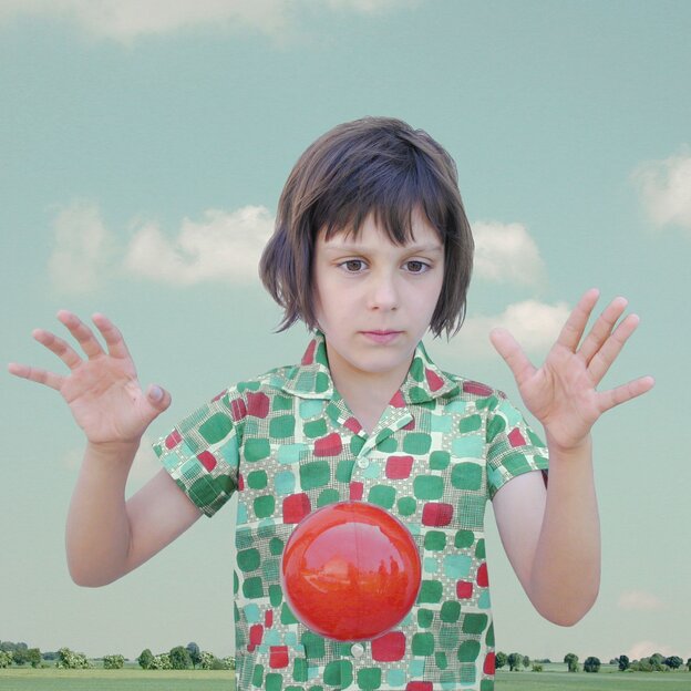 Foto eines Mädchens, das mit einem roten Ball spielt.  Auch auf ihrer Bluse sind rote und grüne Kreise