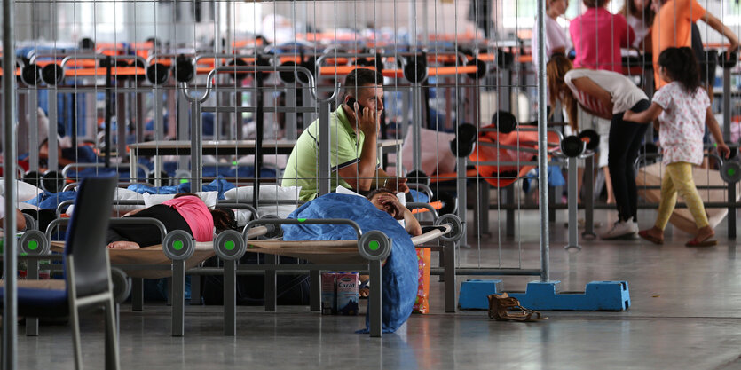 Flüchtling sitzt telefonierend auf einem Bett in Flüchtlingsunterkunft