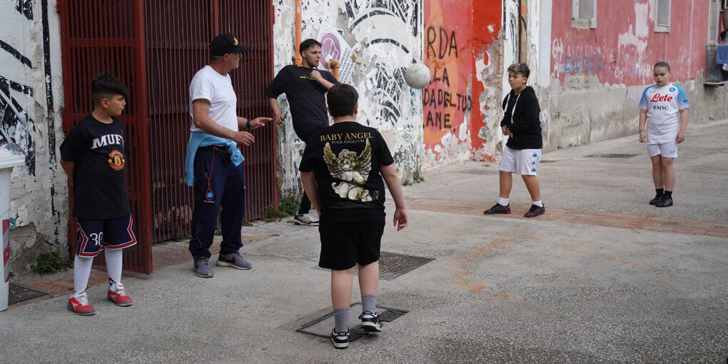 Ein älterer Mann trainiert mit Kindern auf der Strasse Fussball