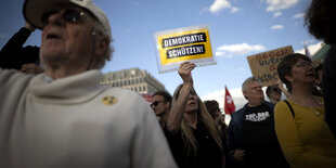 Eine Person in einer Menschenmenge hält ein Schild mit der Aufschrift "Demokratie schützen!" in die Höhe