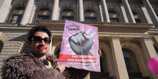 Allessandro hält vor dem Berliner Abgeordnetenhaus ein Plakat mit der Aufschrift "Tuntenhaus bleibt - Save queer Spaces".