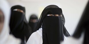 Mehre Personen, die mit Niqab bekleidet sind, sitzen in einem Klassenraum.