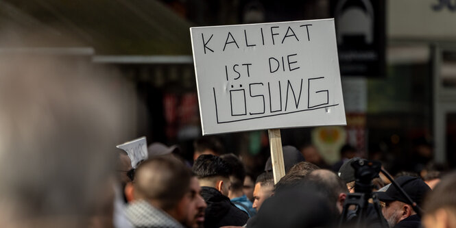 Teilnehmer einer Islamisten-Demo halten ein Plakat mit der Aufschrift „Kalifat ist die Lösung“ in die Höhe.