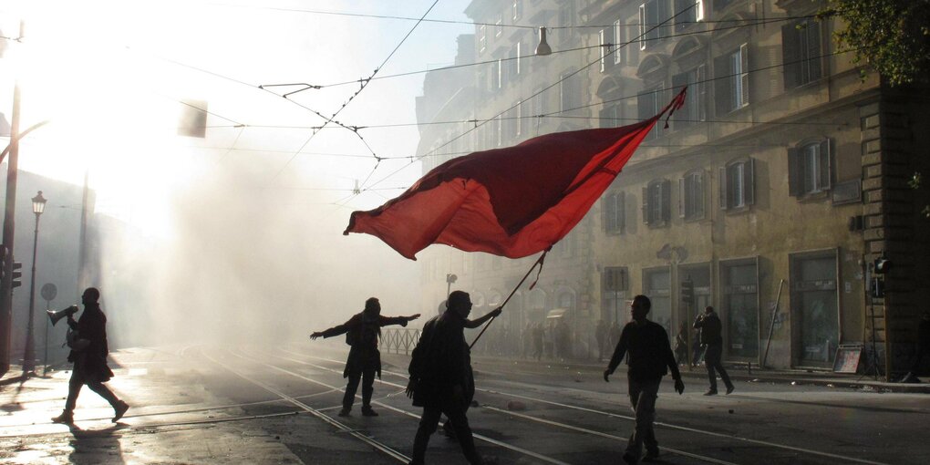 Aufständige schwenken eine rote Fahne in den Straßen von Rom während der Demonstration "People of Europe, rise up!" (deutsch: Völker Europas, steht auf!) gegen die Finanzindustrie 2011.