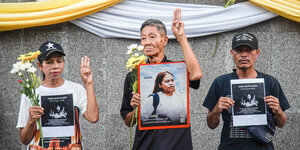 3 Menschen halten Porträts und blumen zum Gedenken, 3 Finger ihrer linken Hand ausgestreckt
