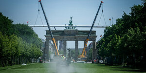 Vor dem Brandenburger Tor ist grüner Kunstrasen verlegt, zwei große Kräne heben einen riesigen Balken an, es wird ein stilisiertes riesiges Fußballtor vorm Brandenburger Tor errichtet