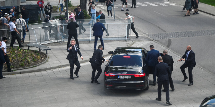 Personenschützer stehen und laufen um einen schwarzen Wagen