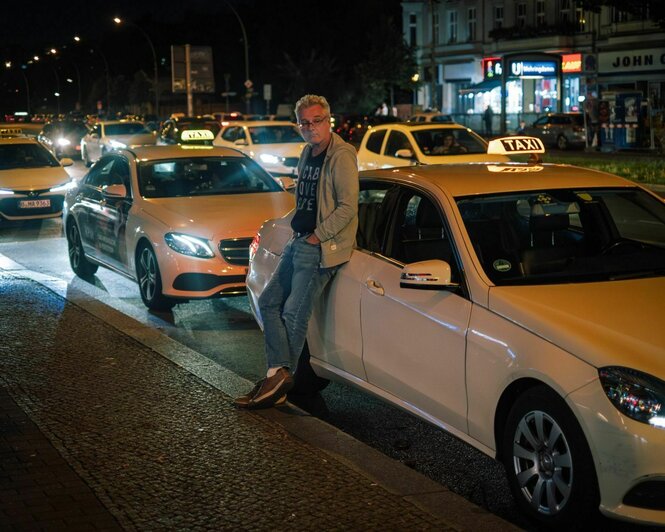 Eine Reihe Taxis am Straßenrand, Uwe Jessen lehnt sich an das vorderste