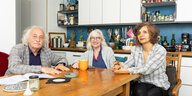 Senioren-WG in Köln - die drei BewohnerInnen - zwei Frauen und ein Mann sitzen an einem gemütlichen Holztisch in der Küche und schauen gut gelaunt in die Kamera