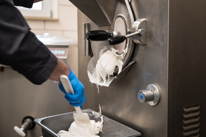 Detailaufnahme der Eismaschine, aus der gerade eine Menge Vanilleeis fließt