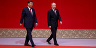 Xi und Putin gehen vor einer roten Wand im Gleichschritt